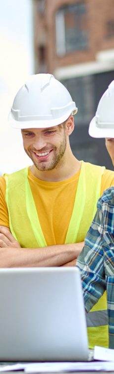 Important information. Three men in protective helmet looking at laptop with interest while standing at construction site during day