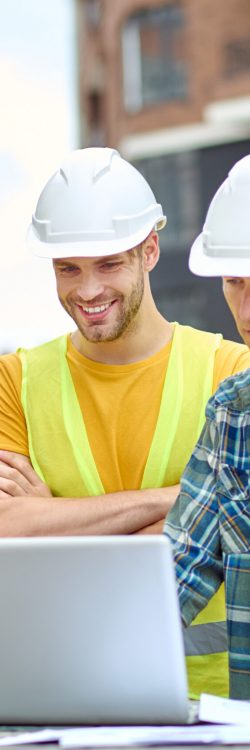 Important information. Three men in protective helmet looking at laptop with interest while standing at construction site during day