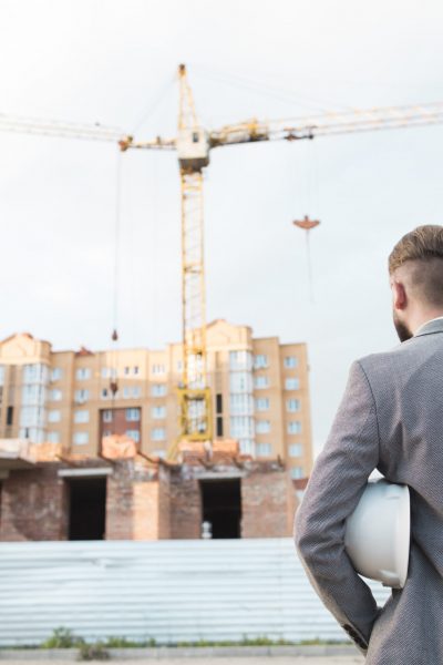 rear-view-male-architect-holding-blueprint-hard-hat-looking-construction-site